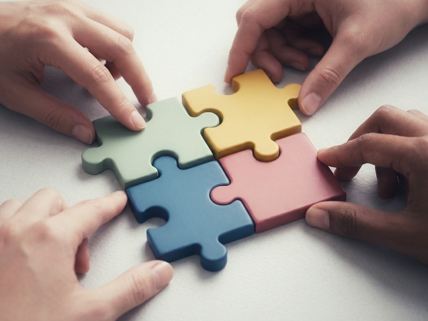 Hands fitting four puzzle pieces together